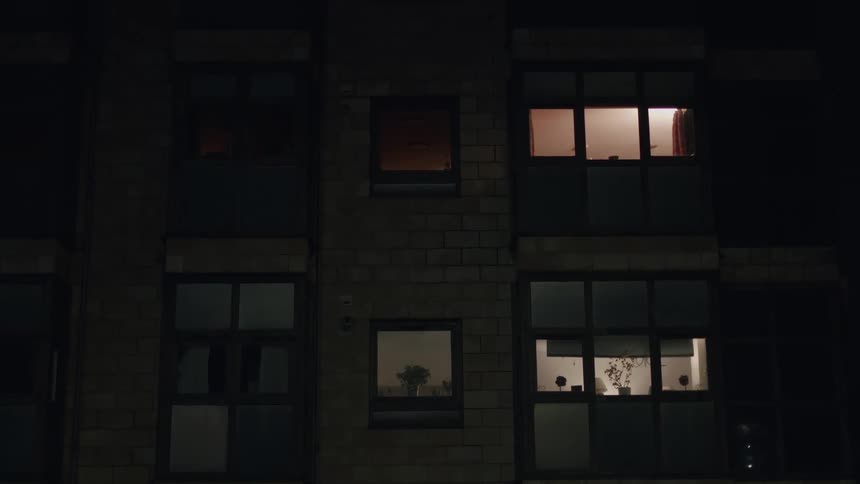 Static shot of a modern apartment building's exterior at night, with several windows illuminated