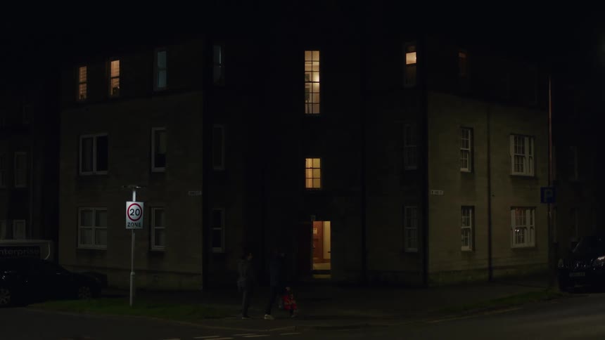 Two people walk across a quiet street at night in front of apartment building