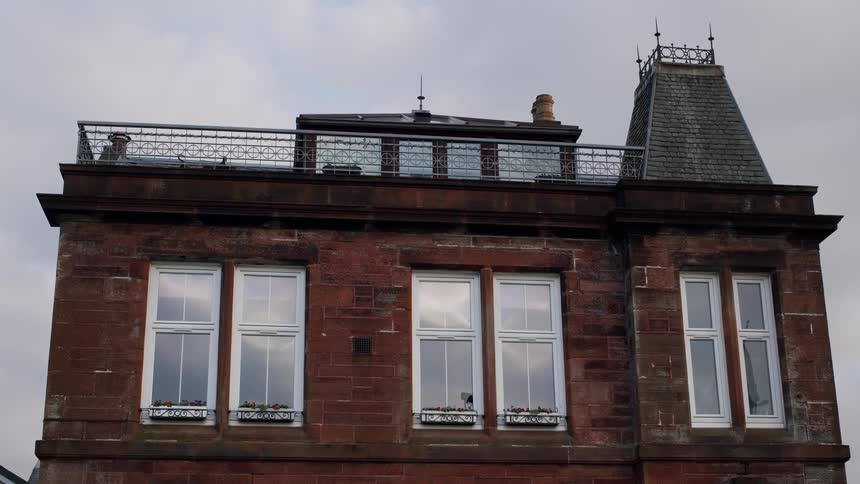 A static shot of a red brick building with a rooftop balcony and white windows under a cloudy sky