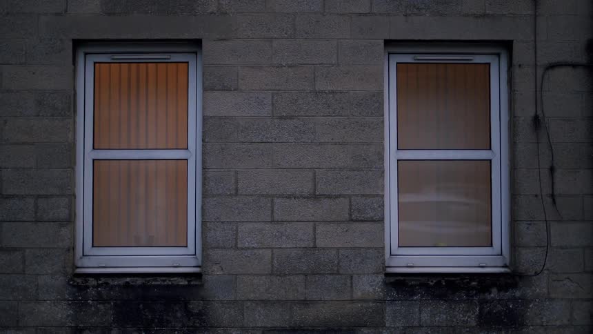 Warmly lit windows on a brick building at dusk show reflections of passing traffic