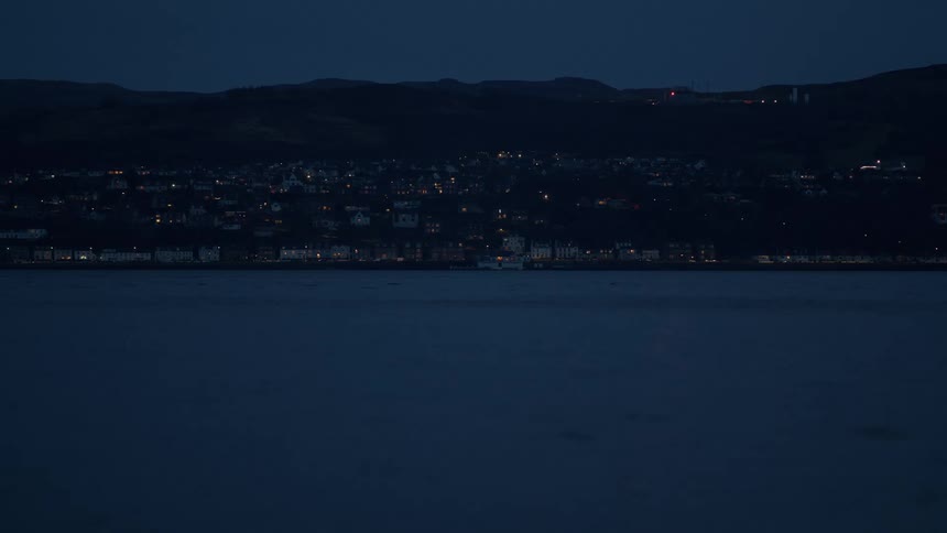 A quiet coastal town glows with lights across the dark water at dusk