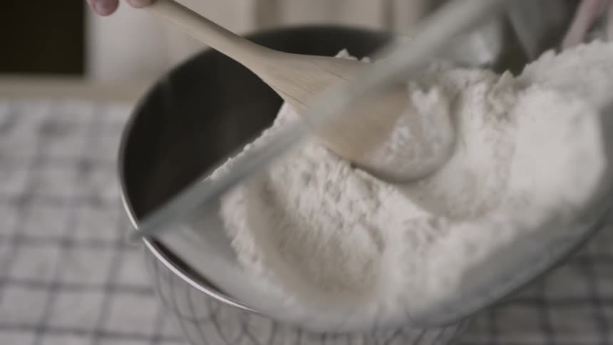 A person spoons flour into a mixing bowl