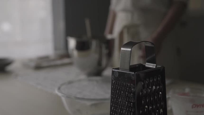A chef stands by a counter and reaches for a grater