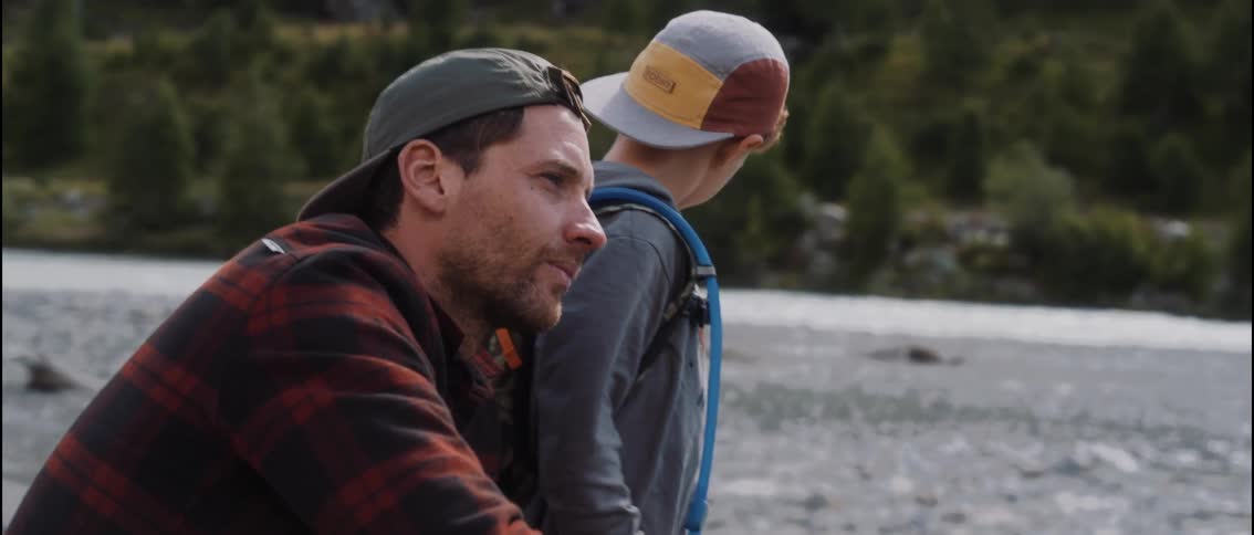 A father and son share a quiet, bonding moment by a rocky river during a hike in the wilderness