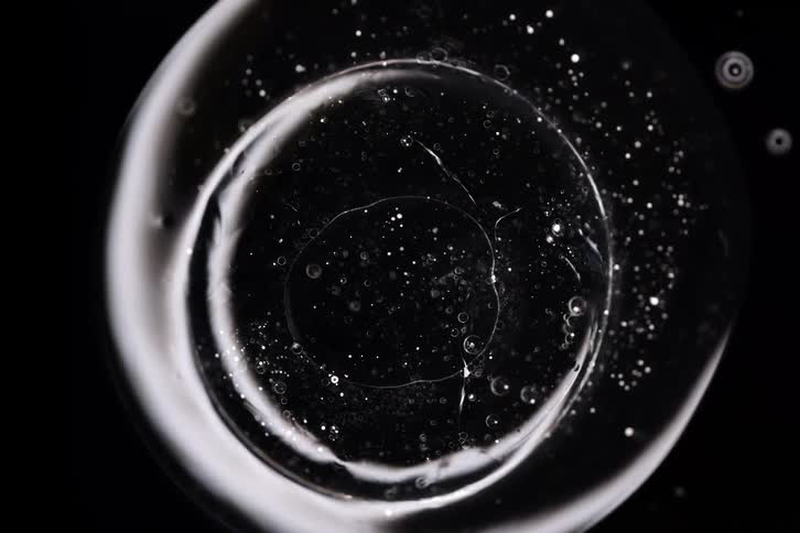 Abstract macro shot of a transparent orb with tiny particles floating inside like a galaxy on a black background