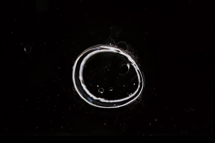 Abstract macro shot of two glowing liquid bubbles slowly morphing and merging into one on a black background