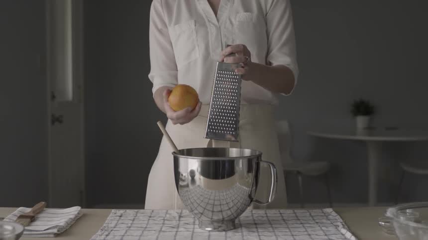 A woman is grating orange zest into a mixing bowl