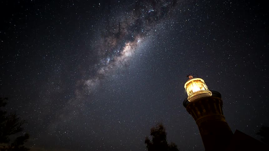 A stunning time-lapse captures the Milky Way galaxy moving across the night sky above a glowing lighthouse