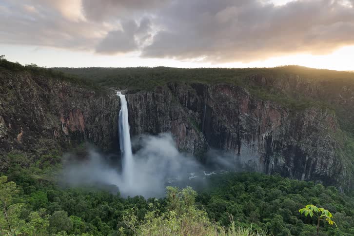 A stunning timelapse shows a powerful waterfall cascading into a misty, jungle-filled canyon as dramatic clouds drift by at sunrise