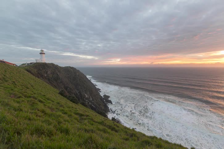 A stunning time-lapse captures the sun rising over the ocean next to a white lighthouse perched atop a grassy cliff