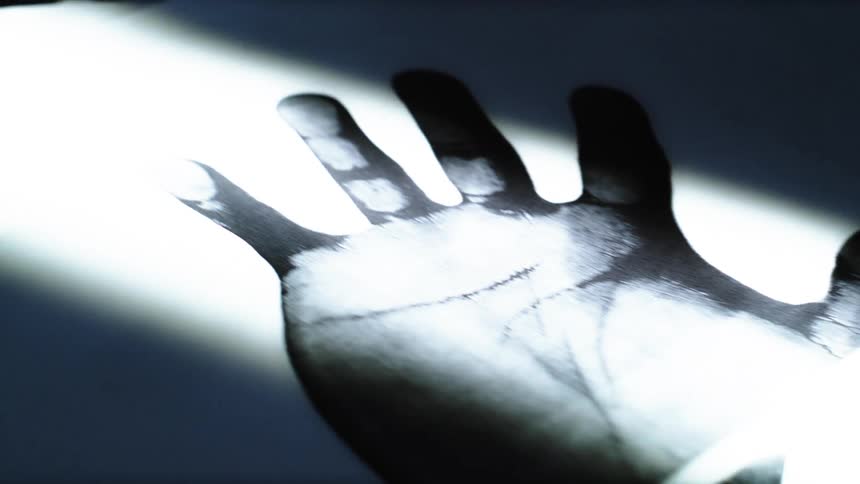 A macro view reveals textures and forms of handprints and silhouettes on paper, illuminated by a single light source