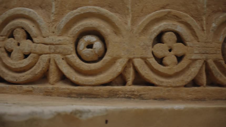 A slow pan reveals the intricate floral and geometric patterns carved into the base of an ancient stone pillar