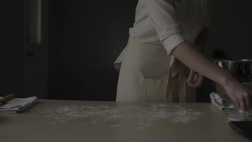 A person sprinkles flour on a table