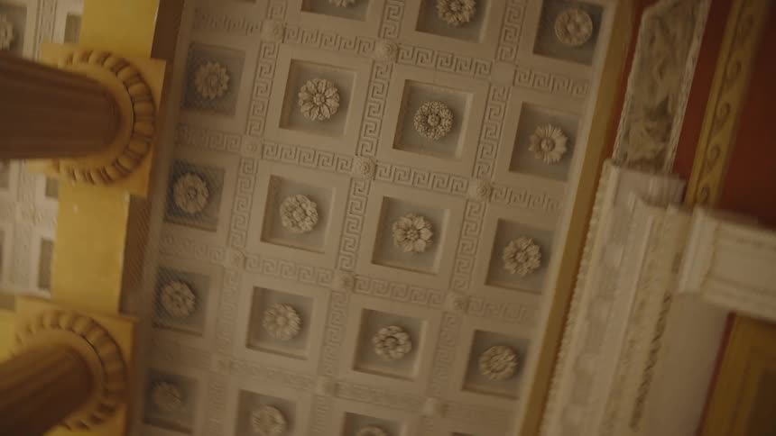 A low-angle, rotating view of an ornate, coffered ceiling with classical Greek key and floral rosette patterns