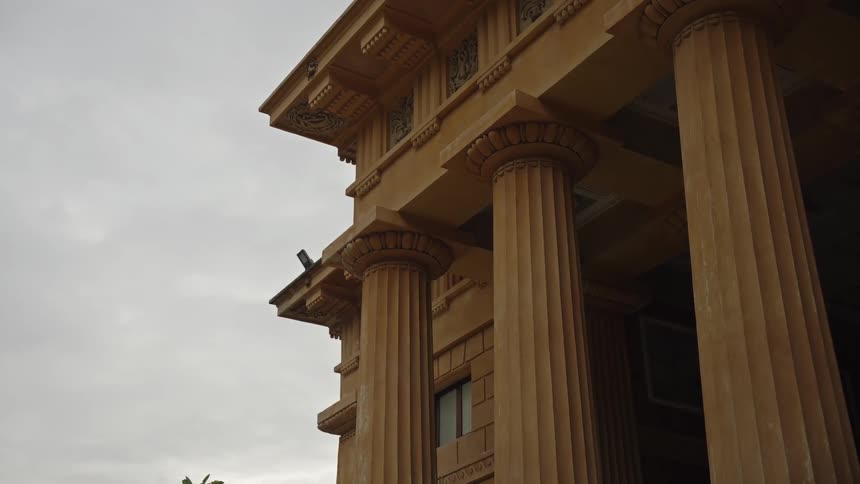 A low-angle static shot of an imposing classical-style building with large columns under an overcast sky