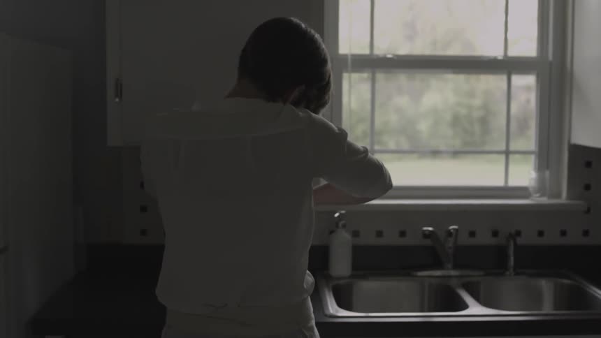 A woman is working to scrape something out of a mixer in her kitchen