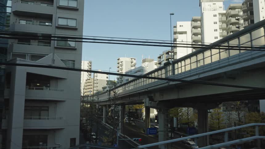 A slow tracking shot from a train reveals the modern architecture and elevated highways of a Japanese city
