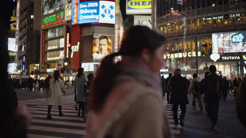 A diverse crowd of pedestrians crosses the famous Shibuya Crossing in Tokyo at night, illuminated by vibrant neon signs in slow motion