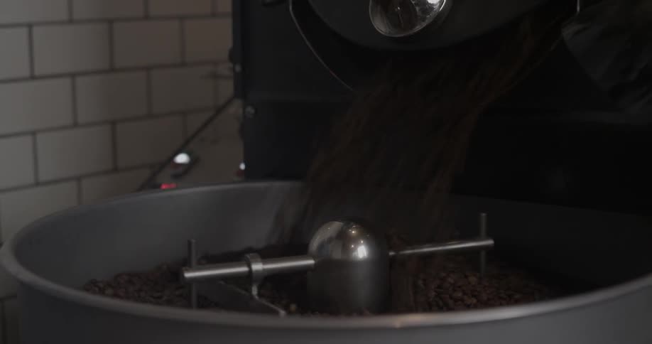 Man in a beanie pours coffee beans into a large grinder