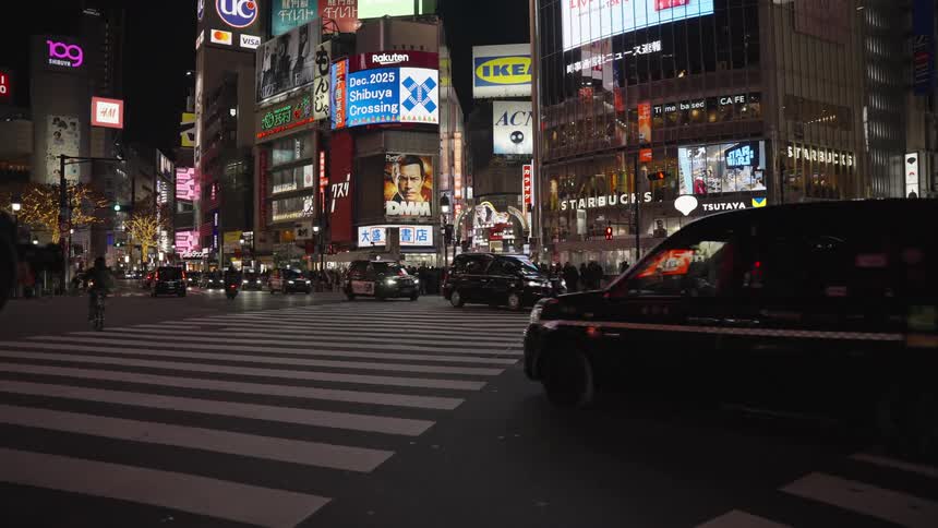 Cars and cyclists navigate the iconic Shibuya Crossing intersection in Tokyo, Japan, as neon signs illuminate the bustling city at night