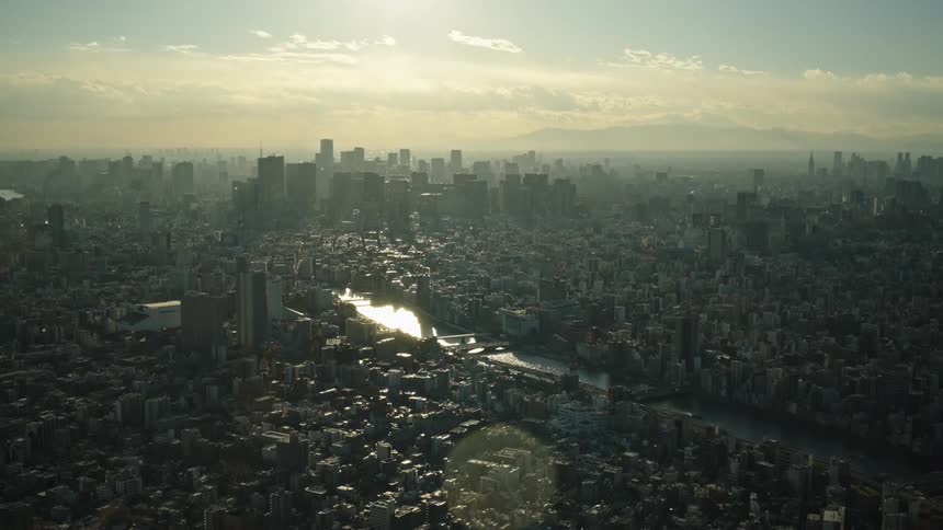 A stunning aerial view of the vast Tokyo cityscape at golden hour, with the sun reflecting off a winding river