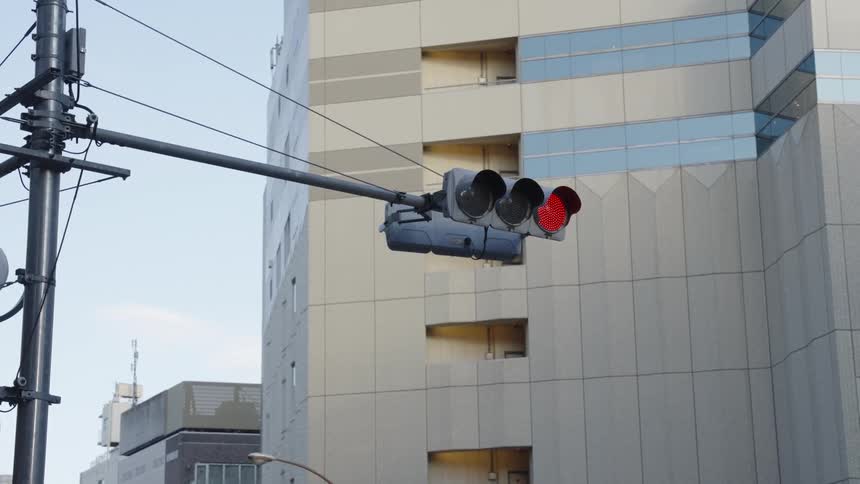 An urban traffic light in Japan switches from red to green with a modern building in the background