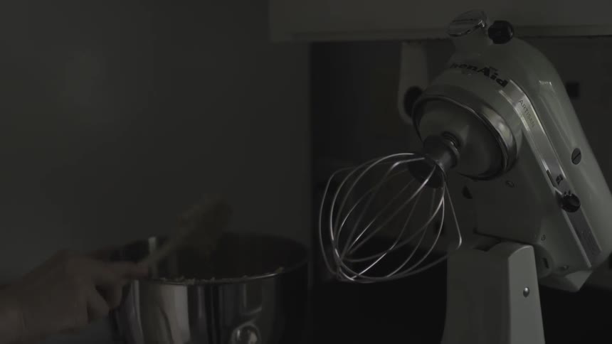 A person's scrapes dough out of a metal bowl with a spatula