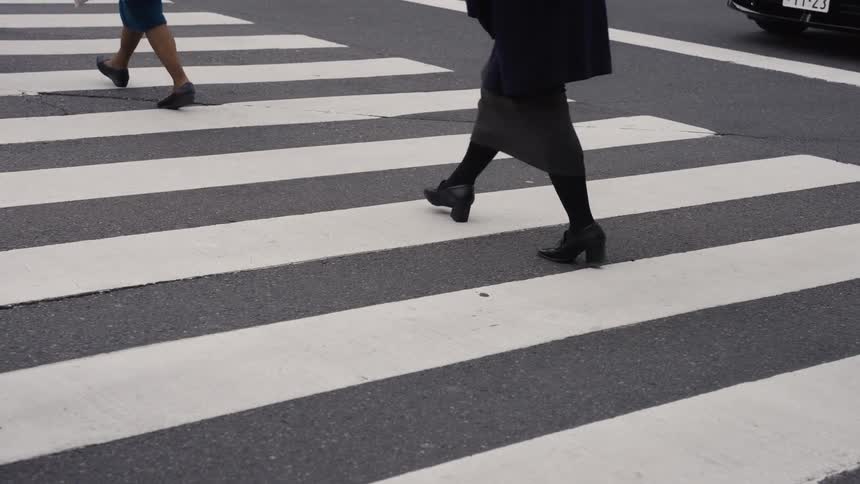 A slow-motion close-up of pedestrians' legs and feet crossing a city street at a crosswalk