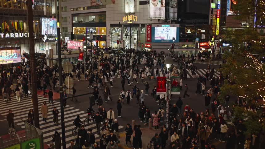 A large crowd of pedestrians navigate the iconic Shibuya Scramble Crossing in Tokyo at night, illuminated by vibrant neon signs