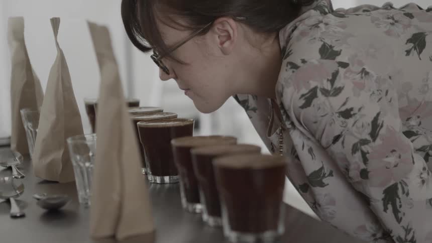 A woman is bending over sniffing coffee in glasses set on a table