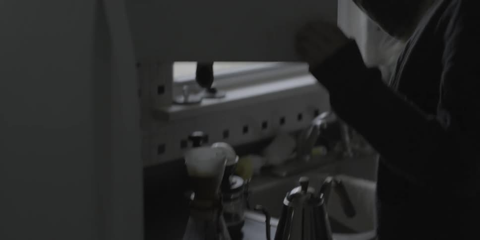 A woman pours hot water into a coffee filter and gets mugs from the cupboard