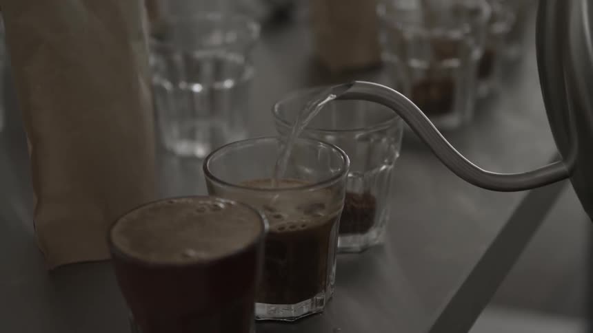 A kettle is pouring coffee into small glasses