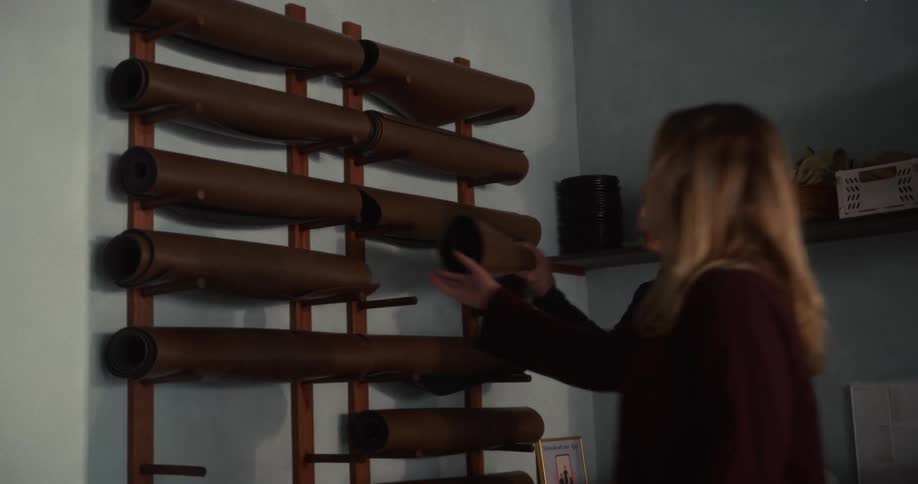 Two women select their yoga mats from a wall rack inside a studio before their class