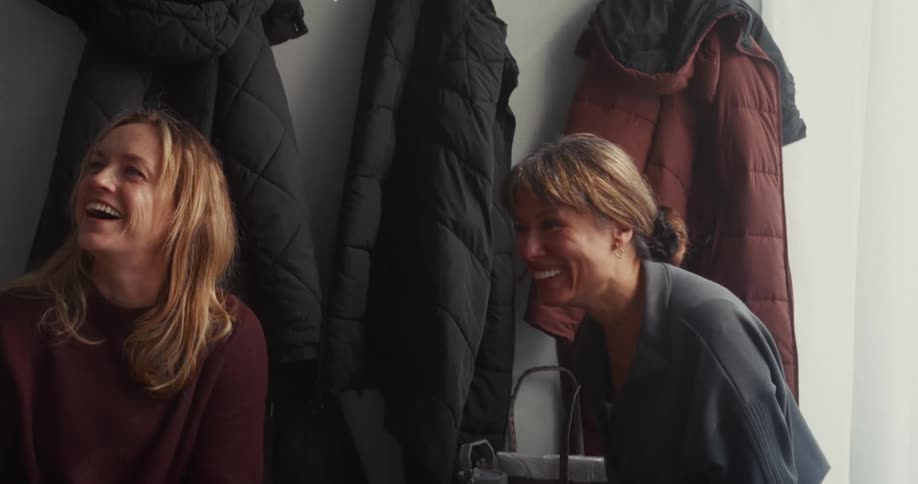 A female instructor laughs and chats with two women in the changing room of a fitness studio