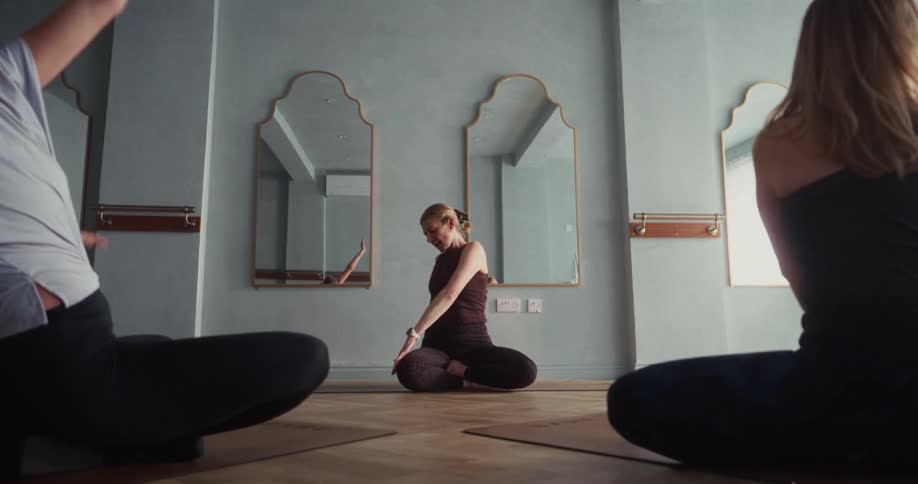Low angle shot of a yoga instructor guiding two women through a seated twist pose in a serene studio