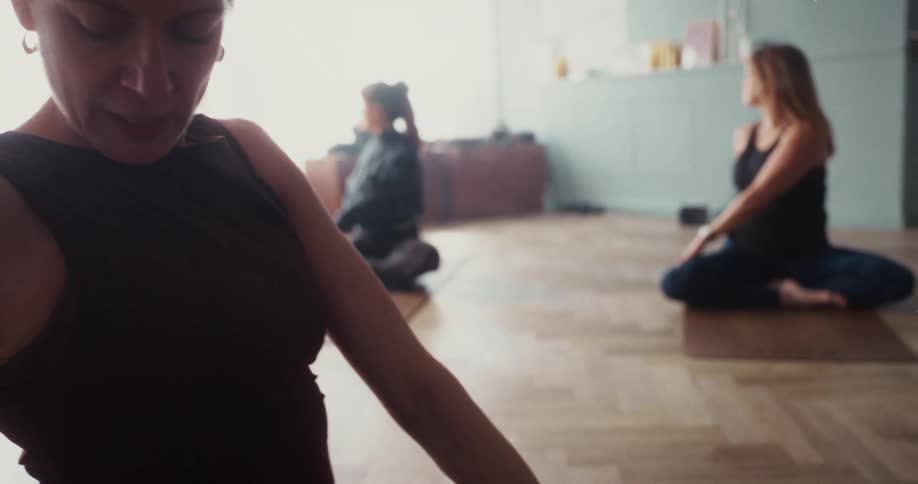 Slow motion close-up of a woman peacefully meditating in a seated pose during a sunlit yoga class