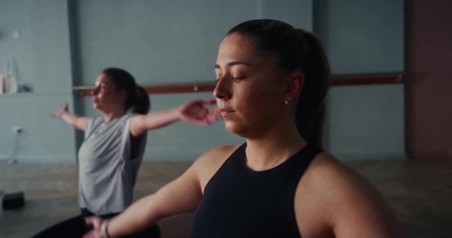 Close up of a focused young woman raising her arms in a mindful yoga pose during a class