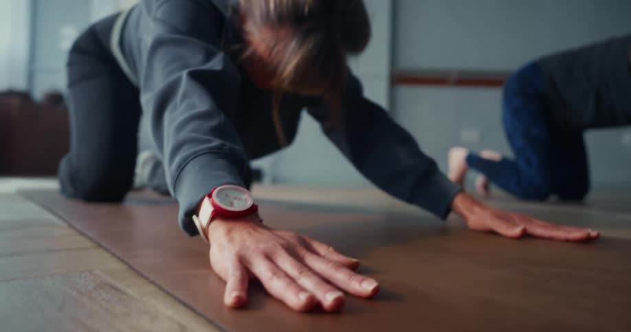 A woman in a yoga studio transitions from a stretching pose into downward dog in slow motion