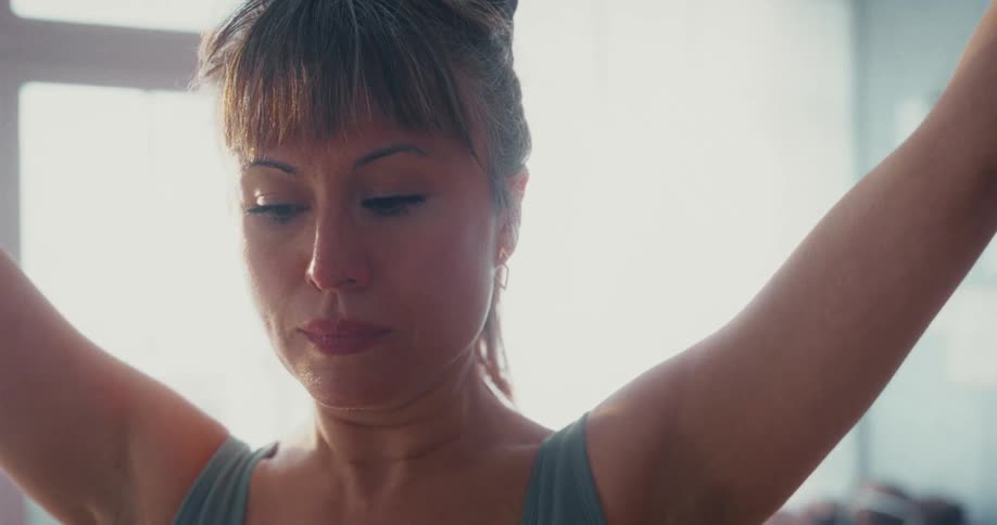 A close-up shot of a serene woman with her arms raised in a meditative yoga pose in a sunlit room