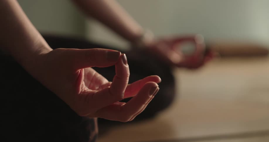 Close-up of a person's hands in a mudra gesture, calmly meditating in a sunlit room