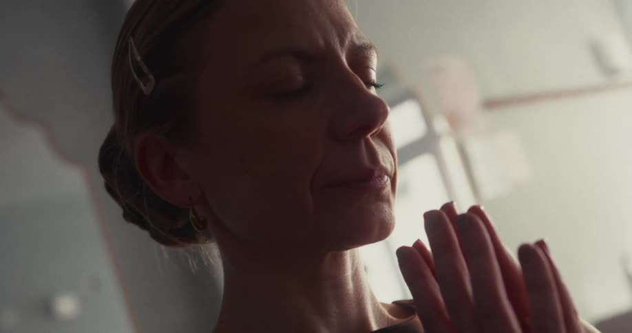 A serene woman meditates with her eyes closed and hands in a prayer pose, finding a moment of inner peace