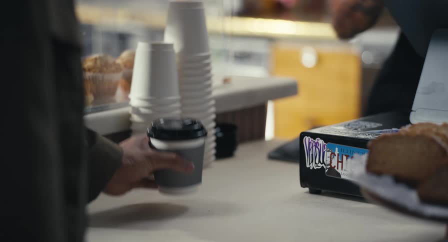 A customer picks up their to-go coffee cup from the counter at a local cafe