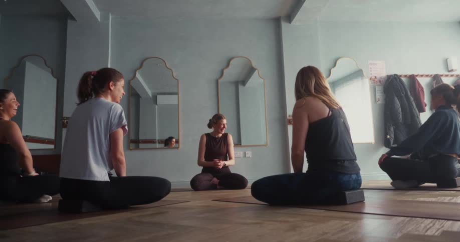 A yoga instructor and her students share a moment of laughter while sitting in a circle in a serene studio
