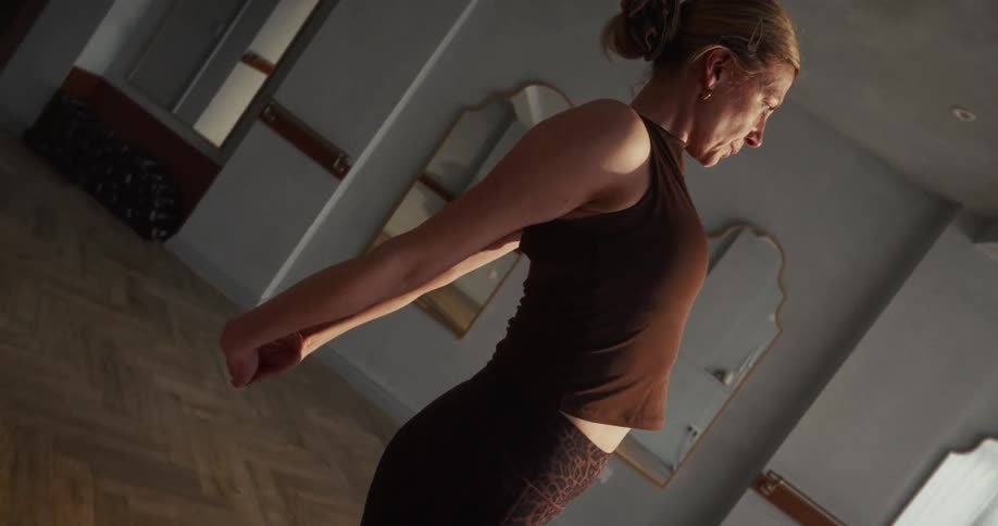 Vertical slow-motion shot of a woman performing a seated shoulder stretch during her yoga practice in a studio