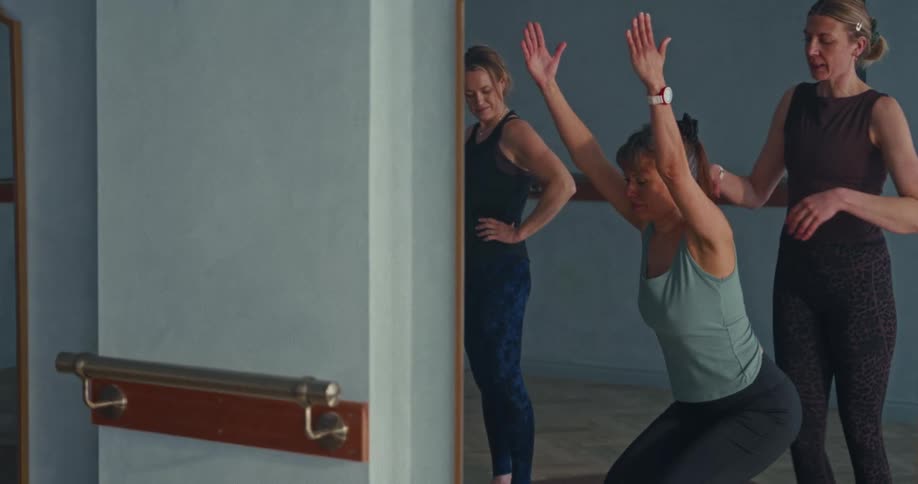 A pilates instructor helps a student perfect her form during a small group class in a fitness studio