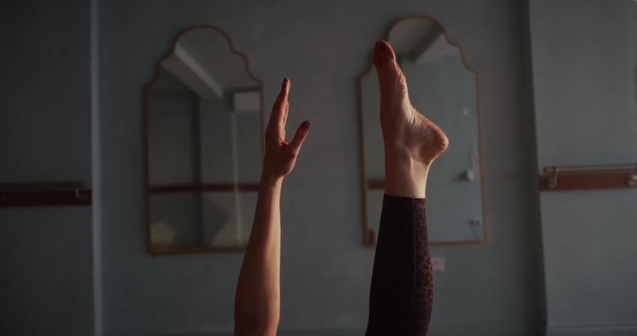A close-up of a woman's leg and arm extended upwards while holding a steady yoga pose in a tranquil studio