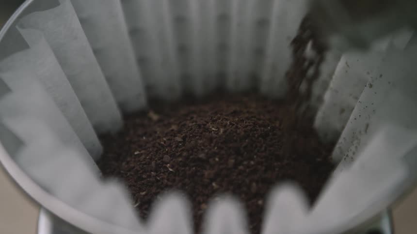 Coffee grounds being poured into a white coffee filter
