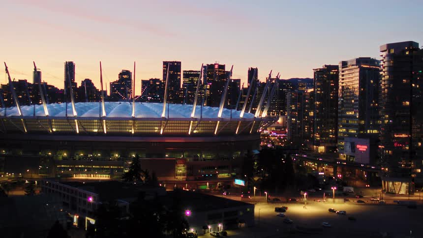 An aerial view of the iconic BC Place stadium and the Vancouver city skyline illuminated against the beautiful dusk sky