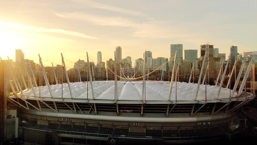 A stunning aerial shot reveals the iconic BC Place stadium and Vancouver's downtown skyline during a spectacular golden hour sunset