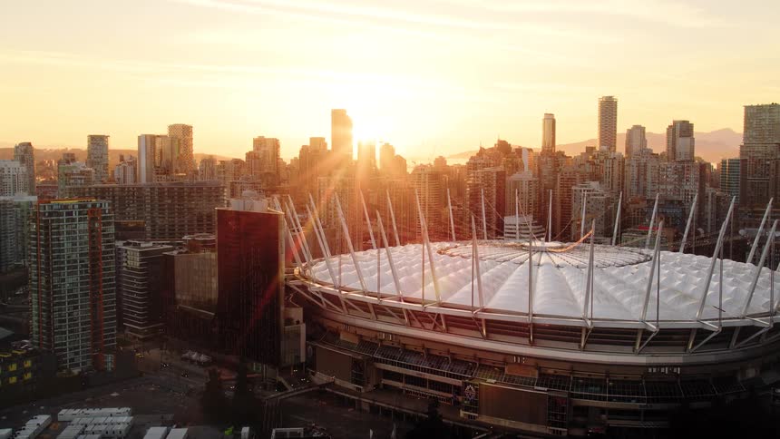 A cinematic aerial shot reveals BC Place stadium and the Vancouver skyline glowing in the beautiful light of a golden sunset